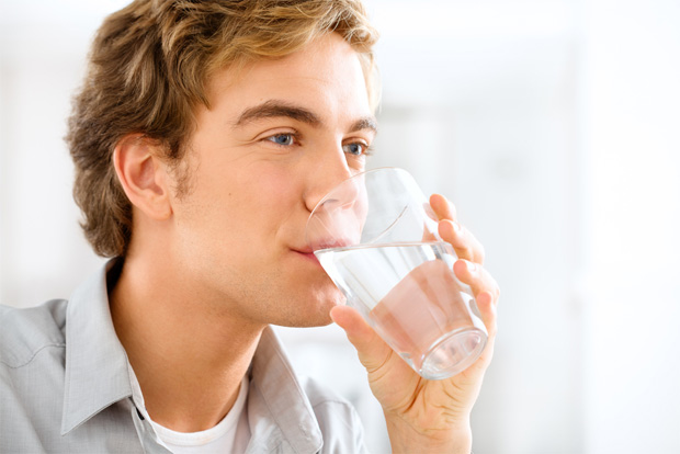 Молодой парень пьет воду из стакана
