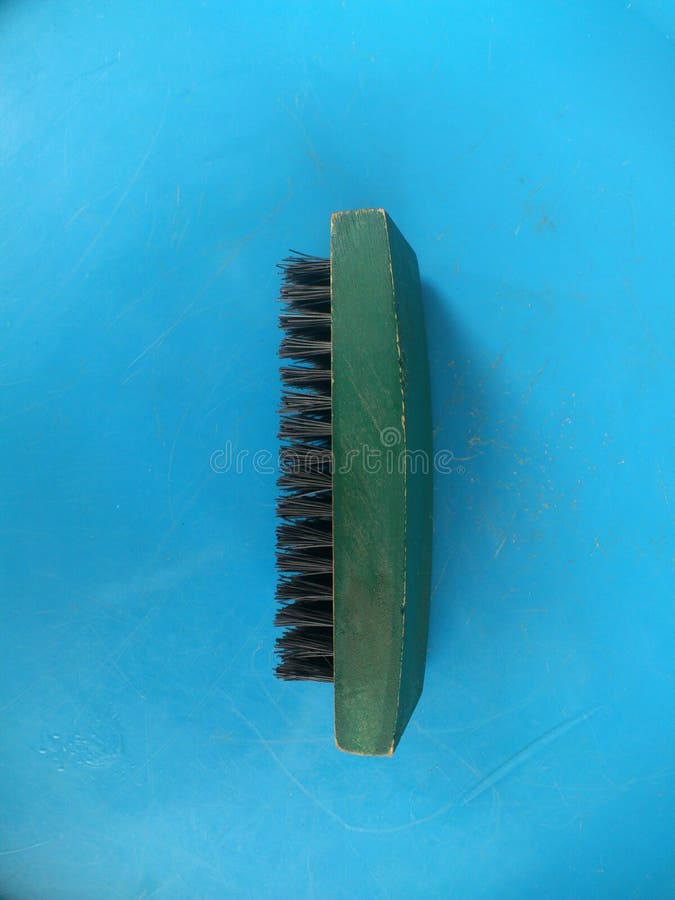 BRUSH HEAD ON A BLUE BACKGROUND. This obviously green brush head with black teeth is exposed on a blue background stock photo
