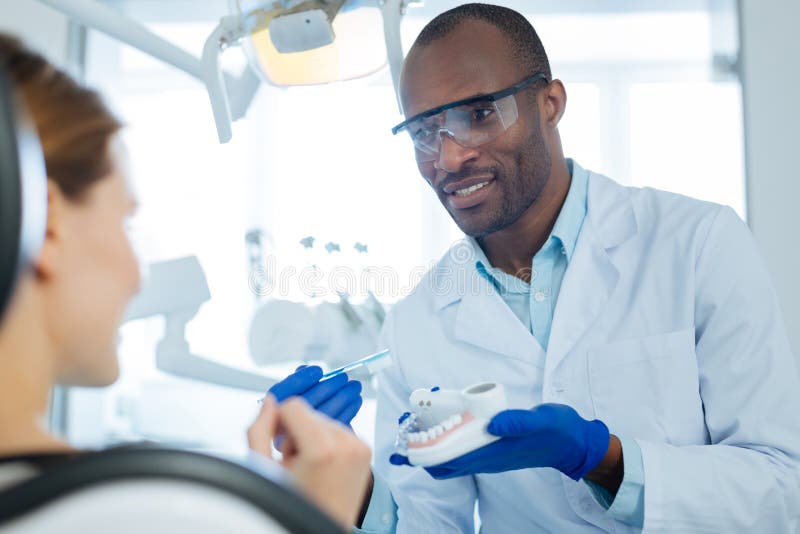 Cheerful man teaching his patient correct teeth-brushing technique. Best technique. Pleasant charming young dentist teaching his patient correct teeth-brushing stock photography
