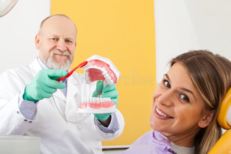 Correct method of brushing teeth. Mature male dentist showing how to brush teeth correctly to female patient royalty free stock photo