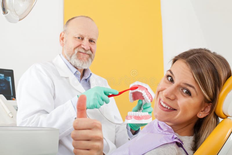 Correct method of brushing teeth. Mature male dentist showing how to brush teeth correctly to female patient, thumbs up royalty free stock photo