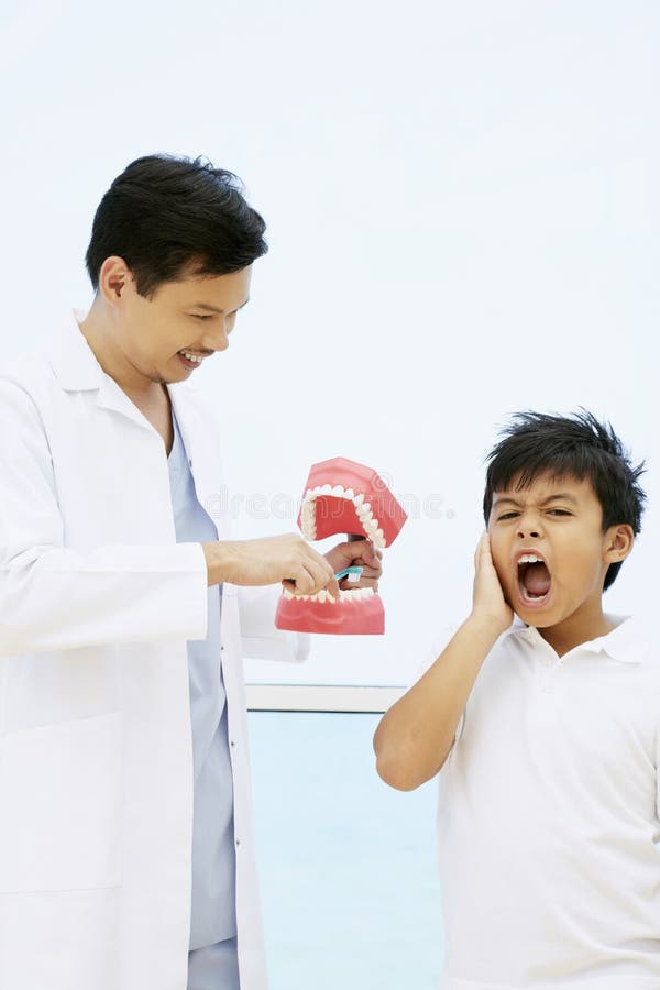 Dentist showing the correct way to brush teeth, boy with toothache. Conceptual image.  stock photo