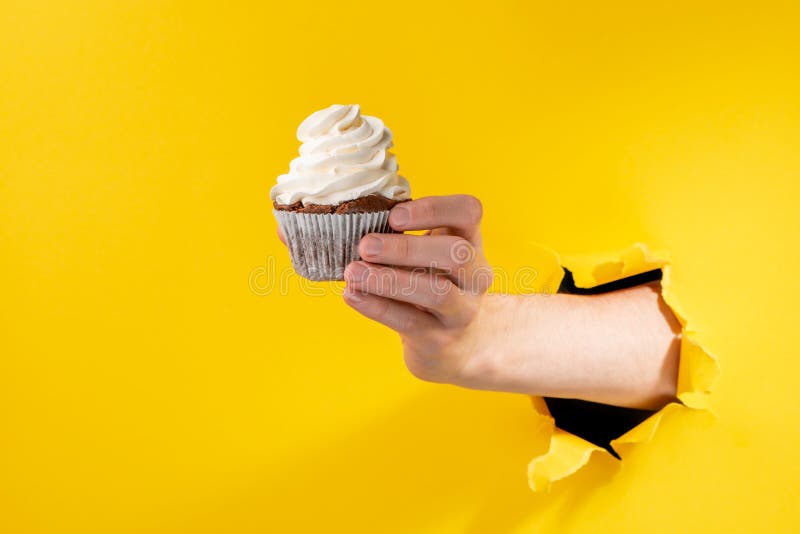 Hand giving a cupcake through torn yellow paper background stock photography