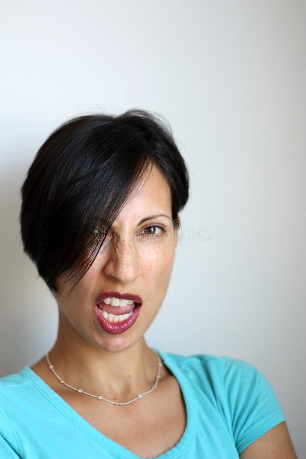 Latina Sneer. Latina with short cropped brunette hair. Side part covers right eye slightly. Scrunching up nose, with mouth parted open, making sneer expression stock images