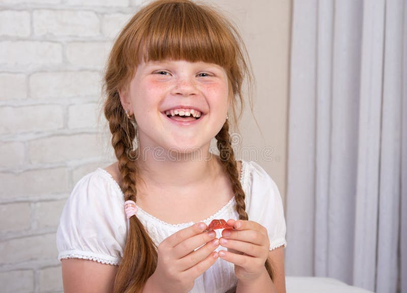 Little red-haired girl in a white dress holds a plate in her hands to correct a bite of teeth. Little red-haired girl in a white dress holds a plate in her hands stock photo