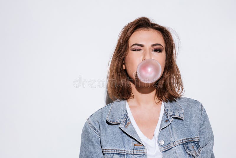 Playful lady blowing bubble with chewing gum. Image of a young playful lady dressed in jeans jacket standing isolated over white background while blowing bubble stock photo