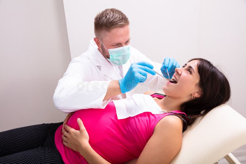 Pregnant Woman Having Teeth Examined At Dentists. A Male Dentist Treating Teeth Of Young Pregnant Woman Patient Lying In Clinic royalty free stock image
