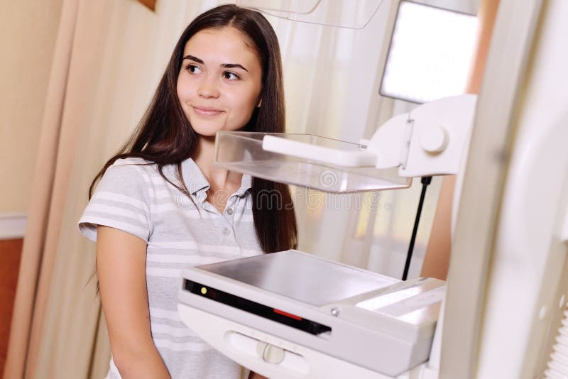 A pretty young girl near a mammographer. An X-ray machine with the help of which breast examinations are performed to prevent or detect tumors and breast stock photography A pretty young girl near a mammographer. An X-ray machine with the help of which breast examinations are performed to prevent or detect tumors and breast stock photography