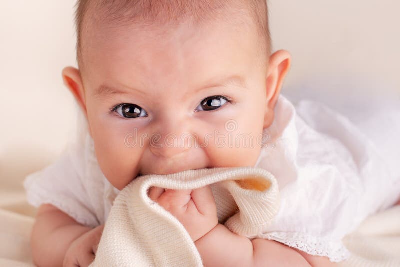 Small cute funny baby infant teething with face expression hands and fingers in mouth. Sore gums soothe close up portrait stock image