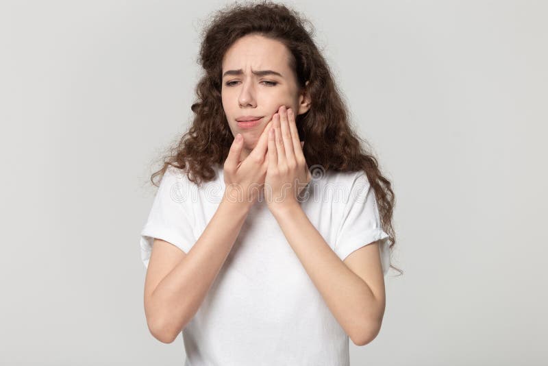 Unhappy young girl touch cheek suffering from tooth pain. Stressed young female isolated on grey studio background touch cheek suffer from toothache, unhappy royalty free stock image