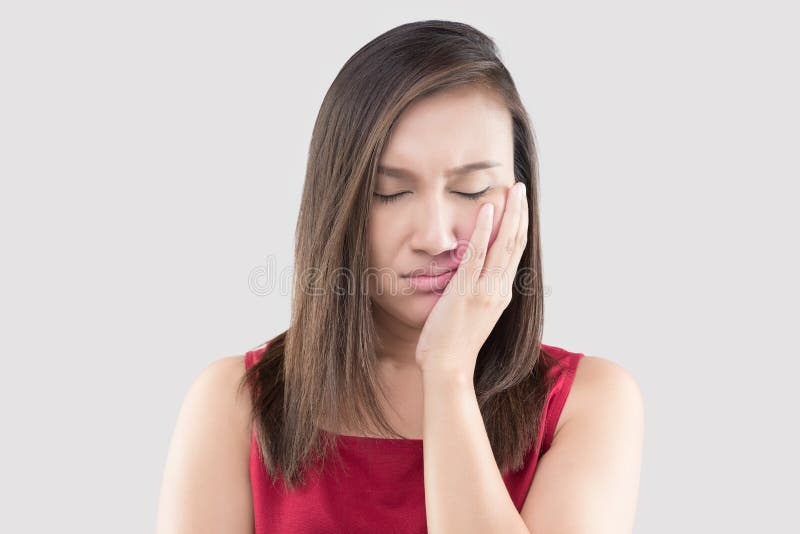 Suffering from a toothache. Suffering from a toothache, Asian woman wearing a red shirt suffering from a toothache while standing against a grey background stock photo