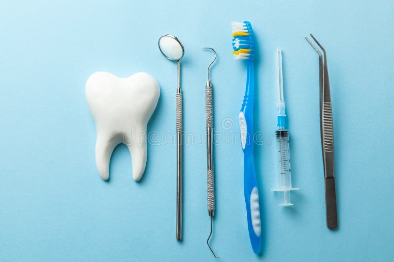 Tooth and dental instruments on blue background. Dental treatment. Dentist tools mirror, hook, tweezers, syringe and toothbrush royalty free stock photography