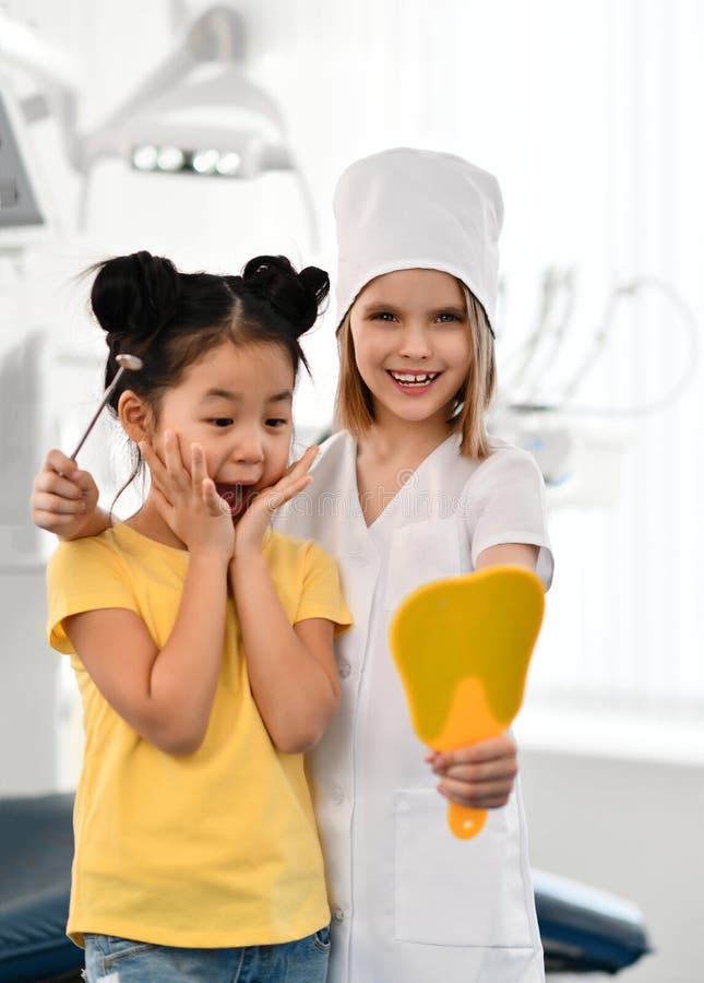 Two kids girls play dentist and happy patient in dental office. Patient is amazed by her healthy teeth stock image