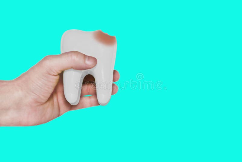 White tooth model in hand with damage from caries on a turquoise background. royalty free stock photos
