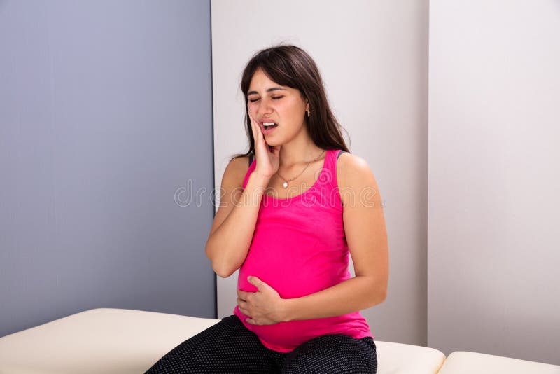 Pregnant Woman Suffering From Toothache In Clinic. Young Pregnant Woman With Painful Expression Suffering From Toothache In Clinic royalty free stock images